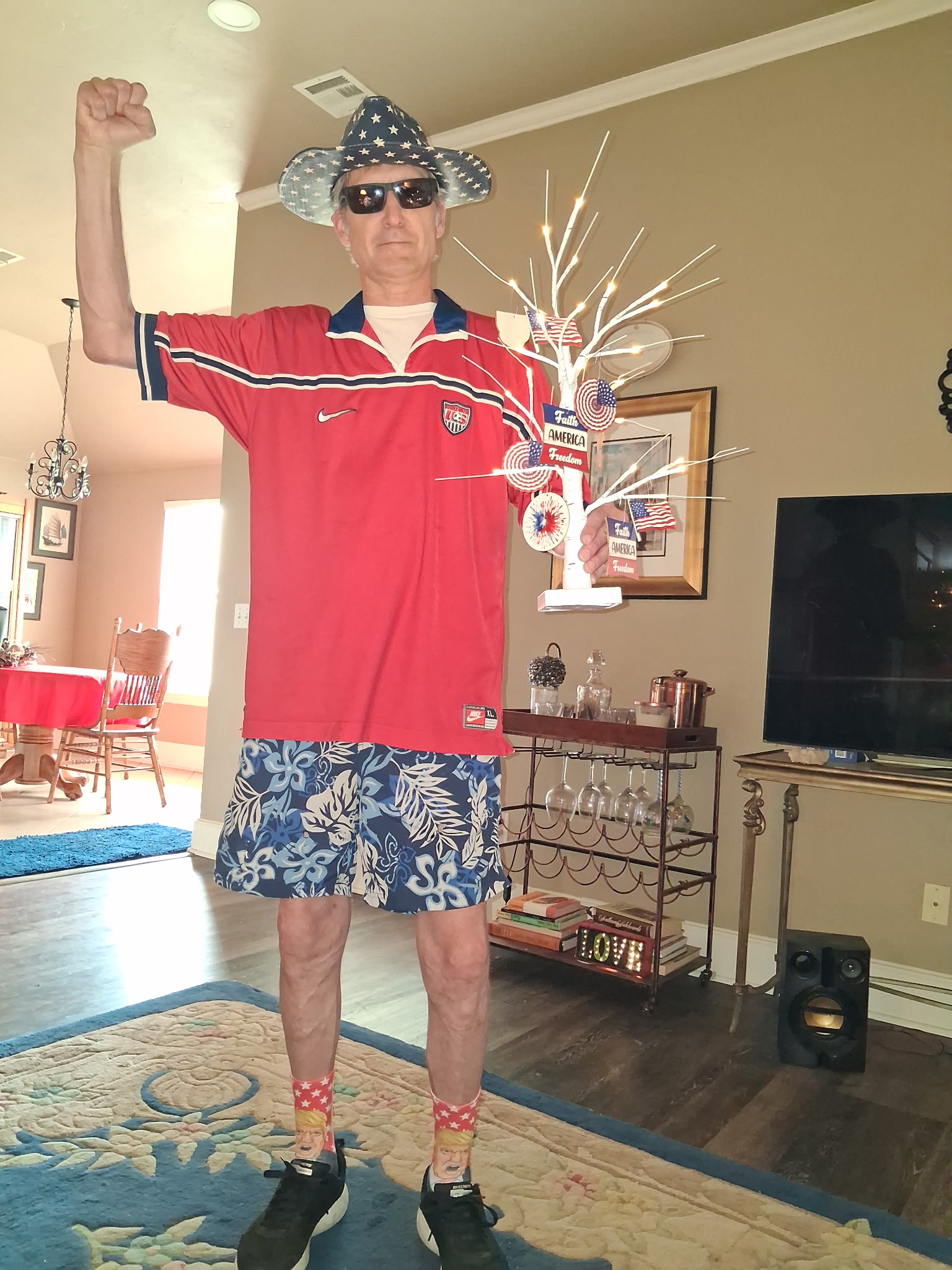 Brian Pritchett standing proudly in patriotic attire, fist raised, in his living room decorated for the Fourth of July